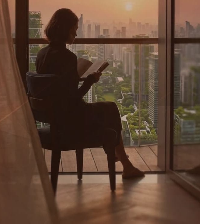 Resident reading beside a floor-to-ceiling window at SkySOLIS with a hazy city skyline